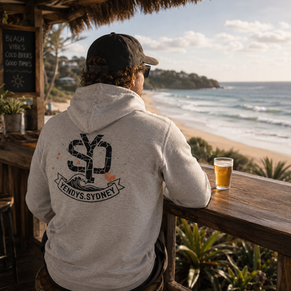 Person wearing a hoodie with a logo, sitting at a beach bar with a drink.