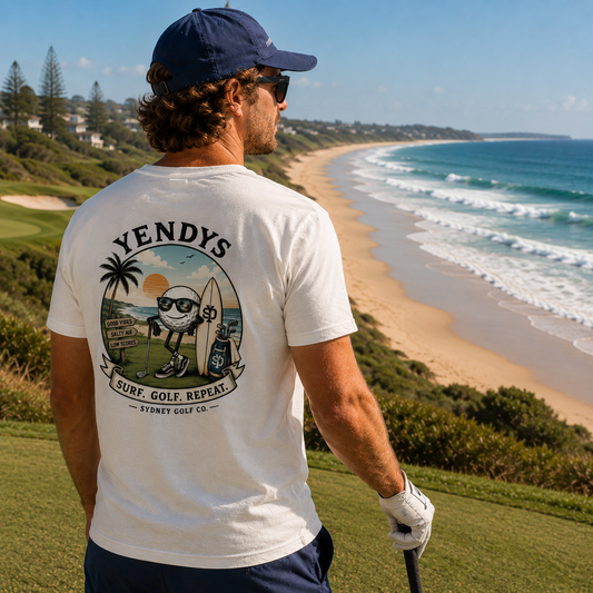 Man wearing a 'Yendys' t-shirt with a golf and beach design, standing on a golf course with ocean view.